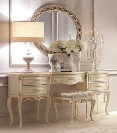 a dressing table with a mirror, stool and flowers on it in front of a lamp