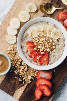 a bowl of oatmeal with sliced bananas and strawberries on the side