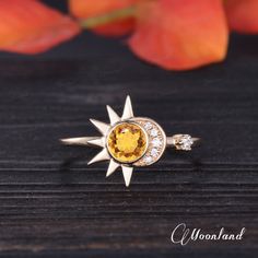 a yellow and white diamond ring sitting on top of a wooden table next to an orange flower