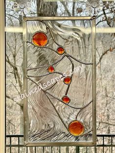 a stained glass window with trees and branches in the background, on a porch railing