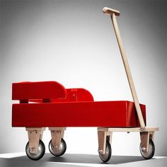 a red wagon with a wooden handle and two wheels on the bottom, sitting in front of a gray background