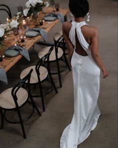 the back of a woman in a white dress standing at a table with flowers and candles