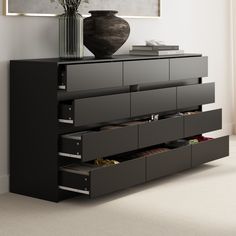 a large vase sitting on top of a black dresser next to a wall with drawers