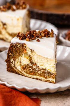 a slice of carrot cake on a white plate with pecans around it and another piece in the background