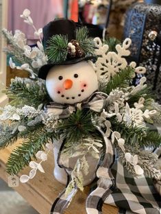 a snowman in a top hat and scarf sitting on a bench with pine branches