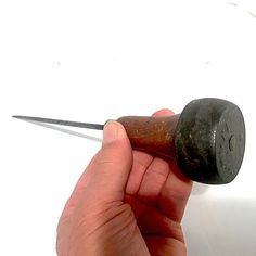 a hand holding a small metal object with a long blade sticking out of it's end