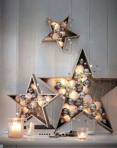 two star shaped christmas decorations on a mantle with candles in front of them and one lit candle