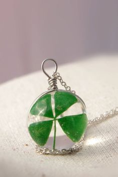 a green four leaf clover necklace on a white surface with a silver ball hanging from the chain