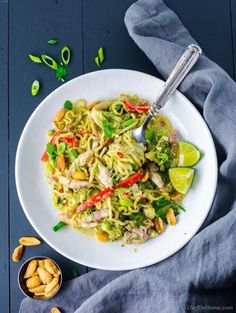 a white plate topped with pasta and veggies next to a bowl of cashews