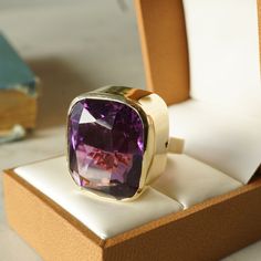 Bezel Set Amethyst Cocktail Ring in 14k Yellow Gold. From the Ancient Egyptians to the Middle Ages and beyond, amethysts have been a highly sought after gemstone with a vast history of international folklore and symbolism. This one of a kind cocktail ring features a 35.41 carat cushion cut purple amethyst finished in 14K yellow gold. The amethyst has a vibrant, dark violet hue. The center stone is bezel set on polished yellow gold band. Composition: 14 Karat Yellow Gold Era: Modern 1970 - Presen Amethyst Cocktail Ring, Contour Wedding Band, Right Hand Rings, Diamond Cocktail Rings, Amethyst Jewelry, Eternity Ring Diamond, Art Deco Diamond, Shop Engagement Rings, Purple Amethyst