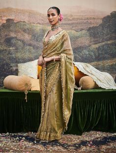 This chic tissue sari is an exquisite embodiment of timeless elegance, featuring delicate dabka work and a gotta patti border adorned with ghumroos. Paired with a chanderi silk blouse embellished with intricate mirror work, this ensemble blends traditional craftsmanship with a modern flair, perfect for elevating your festive look. Diwali Tissue Silk Sharara With Gota Work, Gold Pre-draped Saree With Sheer Dupatta For Navratri, Festive Tissue Silk Sharara With Gota Work, Transitional Tissue Silk Sharara With Dupatta, Festive Tussar Silk Sharara With Gota Work, Eid Traditional Wear With Gota Work On Tissue Silk, Gold Pre-draped Dola Silk Saree With Dupatta, Festive Tissue Silk Sharara With Cutdana, Diwali Mirror Work Pre-draped Tissue Silk Saree