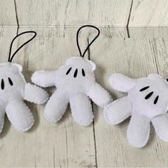 three stuffed ghost ornaments hanging from strings on a white wooden surface with black eyes and hands