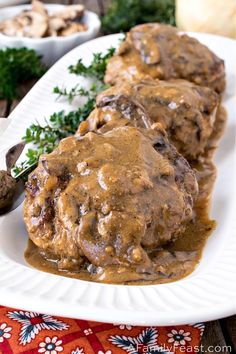 two white plates topped with meat covered in gravy next to mushrooms and parsley