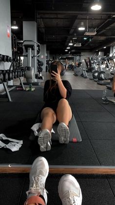 a woman sitting on top of a gym floor talking on a cell phone while holding her hand up to her face