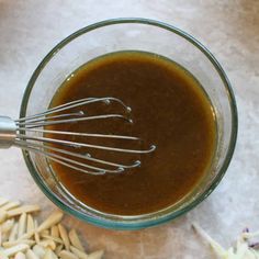 a glass bowl filled with brown liquid next to almonds and an whisk