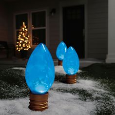 two blue lights sitting on top of snow covered ground in front of a house with a christmas tree