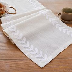 three napkins with white leaves on them sitting next to a cup and saucer