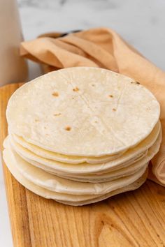 a stack of tortillas sitting on top of a wooden cutting board next to a cup