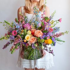 a woman holding a vase filled with lots of flowers