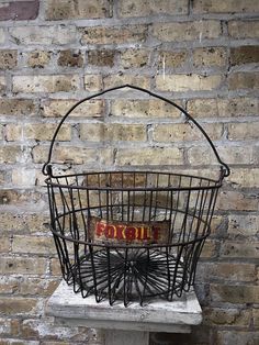 an old metal basket sitting on top of a white table next to a brick wall