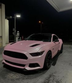 a pink mustang parked in front of a gas station at night with its hood up