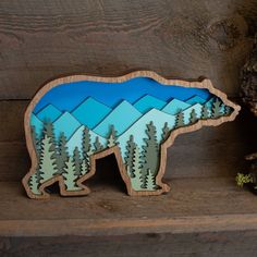 a wooden bear with trees and mountains in the background, on a shelf next to a tree stump