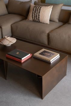 a coffee table with two books on it in front of a brown couch and pillows