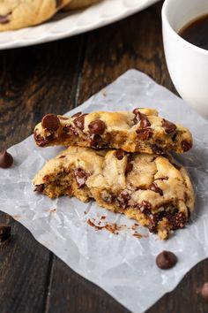 two chocolate chip cookies sitting on top of paper next to a cup of coffee