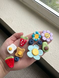 someone is holding out their fingers decorated with different foods and flowers in front of a window