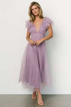 a woman in a purple dress posing for the camera with her hands on her hips