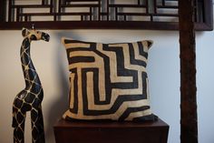 a giraffe statue sitting next to a decorative pillow on a wooden shelf in front of a wall