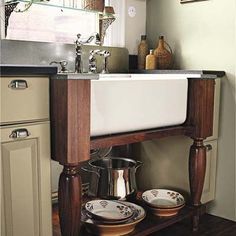 a kitchen sink sitting under a window next to a wooden shelf with dishes on it