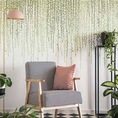 a living room with a chair, potted plants and a wall hanging from the ceiling