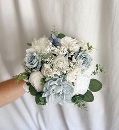 a bridal bouquet with blue and white flowers is held by someone's hand