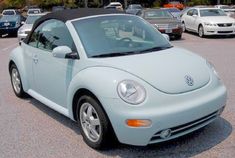 a light blue convertible car parked in a parking lot next to other cars and trucks