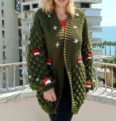 a woman standing on top of a balcony next to a building and wearing a green knitted cardigan