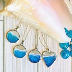 three necklaces with blue and white designs hanging from a shell on a wooden table