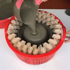 a person pouring cement into a red basket on top of a white table next to other items