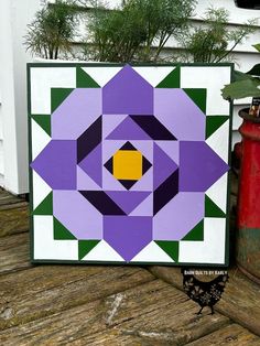 a purple and green quilt sitting on top of a wooden table next to a potted plant