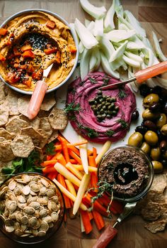 an assortment of food on a table with dips, crackers and olives