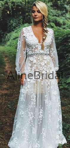 a woman standing in the woods wearing a white dress with sheer sleeves and flowers on it