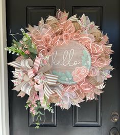 a pink wreath with the word hello on it is hanging on a black front door