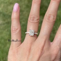 a woman's hand with a diamond ring on top of her finger and grass in the background