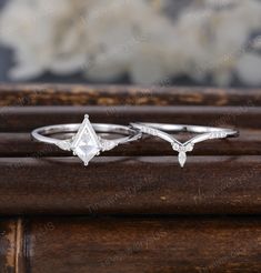 two white gold engagement rings with diamonds on the top and bottom, sitting on a wooden surface