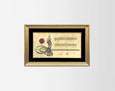 an arabic calligraphy is displayed in a gold frame on a white wall with a black border