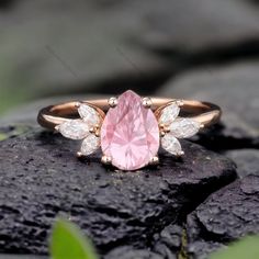 a pink diamond ring sitting on top of a rock next to some green leaves and rocks