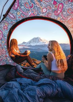 two women sitting in a tent looking out at the mountains and snow capped peaks