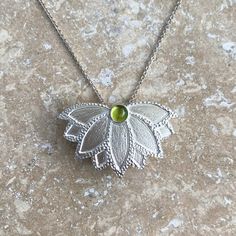 This handmade lotus flower pendant is hand-pierced and texturized from sterling silver. It features a smooth and clear, light green natural peridot gemstone. Peridot is the August birthstone. The pendant measures 1" in height by 1.6" in width and comes with your choice of a sterling silver chain necklace or an Omega necklace. The chain necklace is available in two sizes (16" or 20") and the Omega necklace is 16" with an attached 2" extender. The 16" chain necklace is shown on the model. • Handma Unique Green Flower Pendant Jewelry, Green Sterling Silver Flower Pendant Jewelry, Green Flower Pendant Necklace With Large Pendant, Delicate Green Sterling Silver Necklaces, Green Necklace With Large Flower Pendant, Green Sterling Silver Necklace With Flower Pendant, Delicate Green Sterling Silver Necklace, Silver Flower Pendant Necklace For May Birthstone, Green Sterling Silver Fusion Necklace