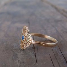 a gold ring with a blue stone in the center on a wooden surface, sitting on top of a piece of wood