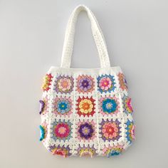 a white crocheted bag with colorful flowers on the front and bottom, hanging from a hook